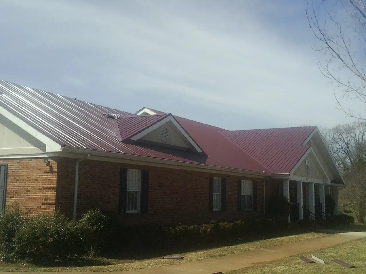 Red metal roof with gabled entries on a long brick building, from a Hail Damage Roof Repair job in South Ozone Park