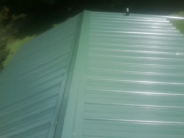 New green metal panels meeting at the ridge of a roof — Flat Roof Repair work by our crew in South Ozone Park