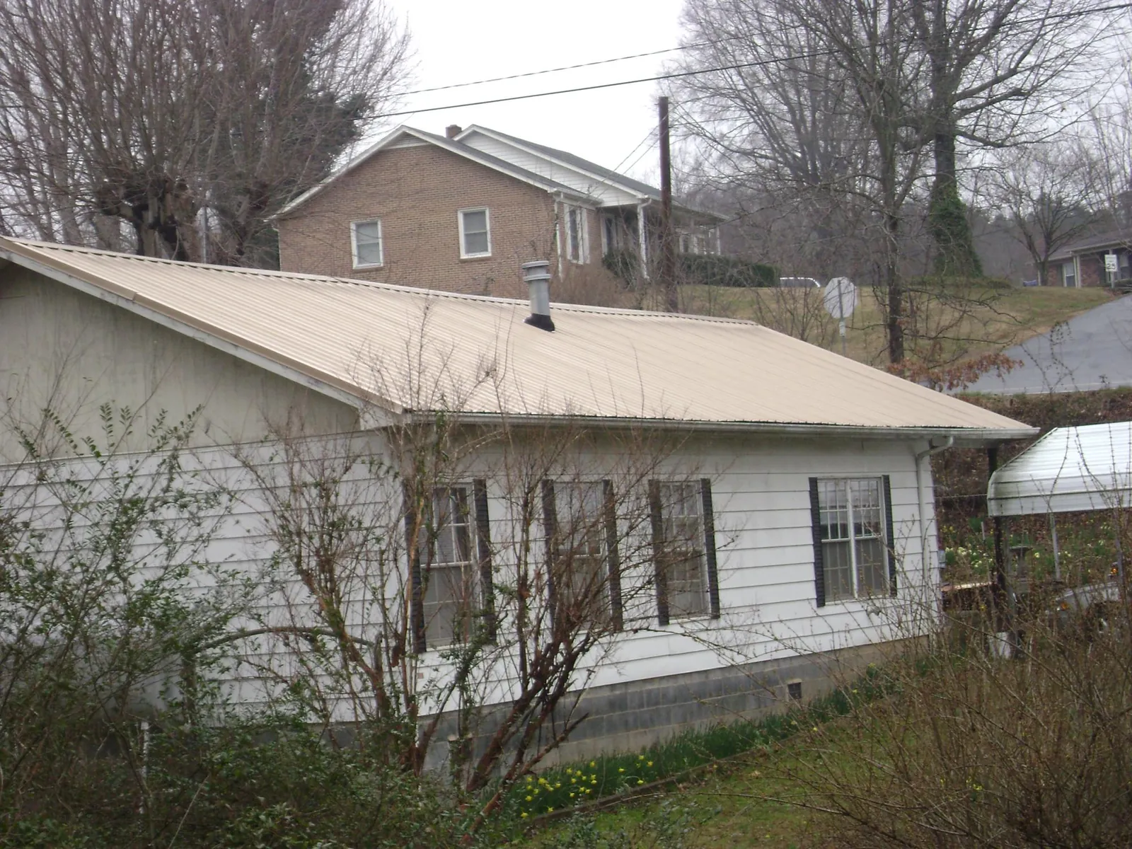 Tan metal roof on a white sided house set into a hillside in South Ozone Park
